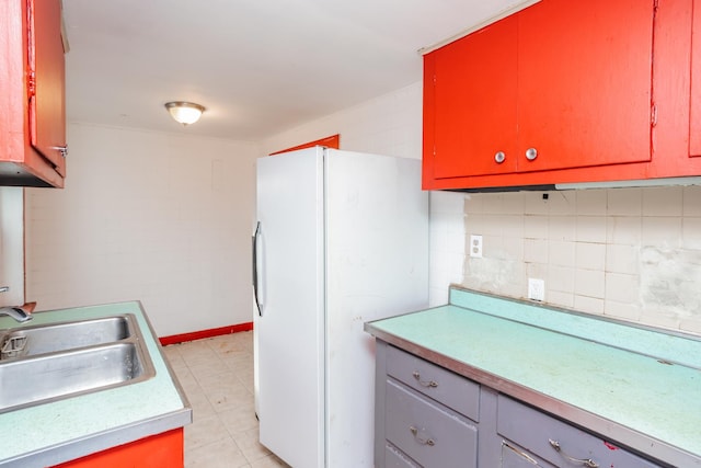 kitchen with backsplash, sink, light tile patterned floors, and white refrigerator