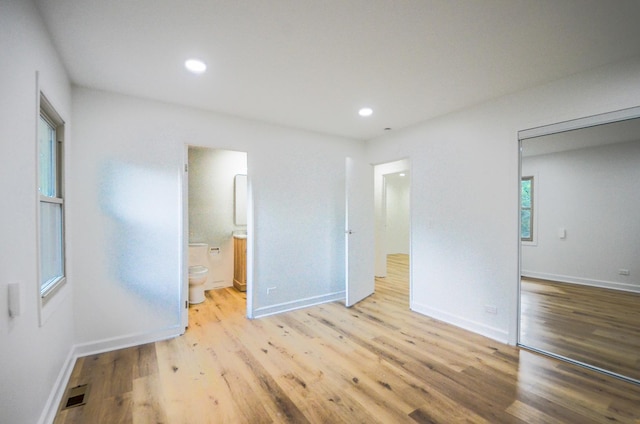 unfurnished bedroom featuring ensuite bathroom, a closet, and light hardwood / wood-style floors