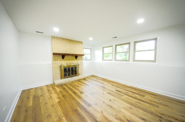 unfurnished living room featuring hardwood / wood-style flooring and a brick fireplace