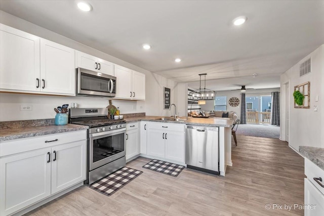 kitchen featuring kitchen peninsula, white cabinets, stainless steel appliances, and decorative light fixtures