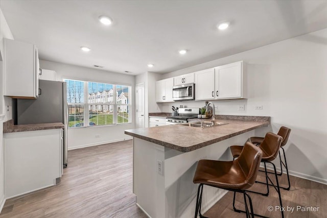 kitchen with kitchen peninsula, white cabinetry, stainless steel appliances, and hardwood / wood-style flooring