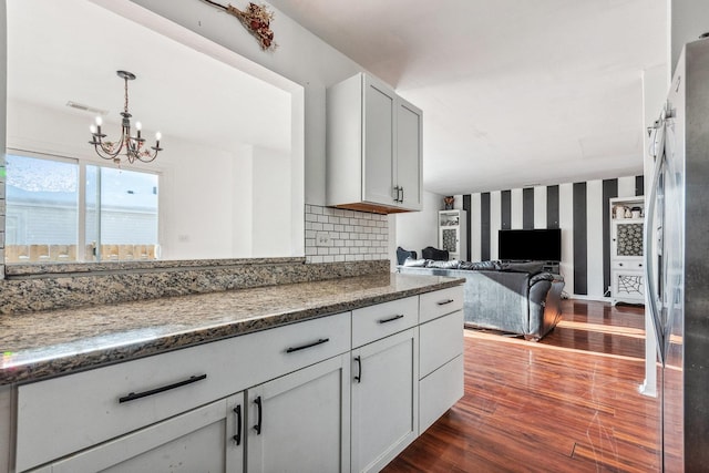 kitchen featuring stainless steel refrigerator, dark hardwood / wood-style flooring, a notable chandelier, backsplash, and decorative light fixtures