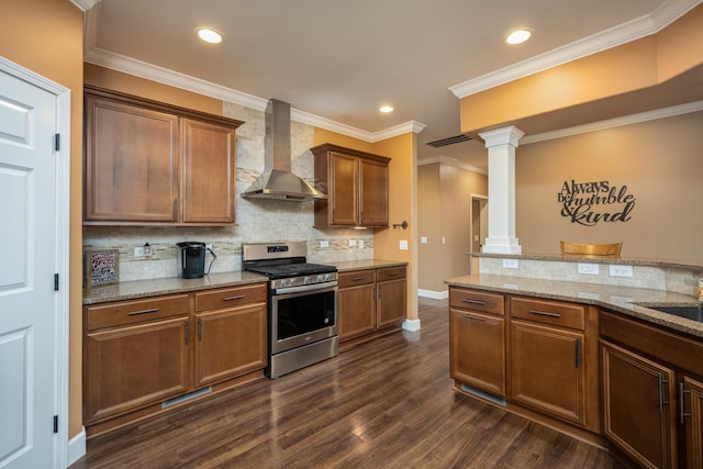 kitchen with stainless steel gas range oven, wall chimney exhaust hood, ornate columns, ornamental molding, and dark hardwood / wood-style flooring