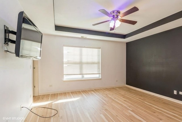 unfurnished room with a raised ceiling, ceiling fan, and light hardwood / wood-style floors