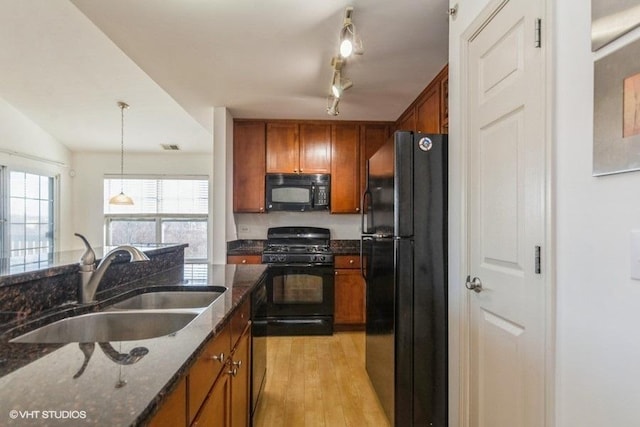 kitchen with sink, hanging light fixtures, dark stone counters, black appliances, and light wood-type flooring