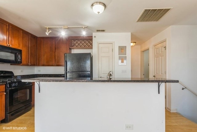 kitchen featuring a kitchen bar, light hardwood / wood-style floors, track lighting, and black appliances