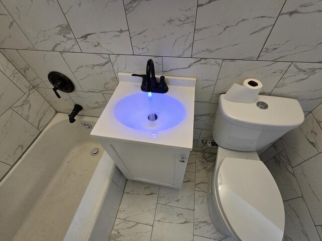 bathroom with vanity, a tub to relax in, toilet, and tile walls