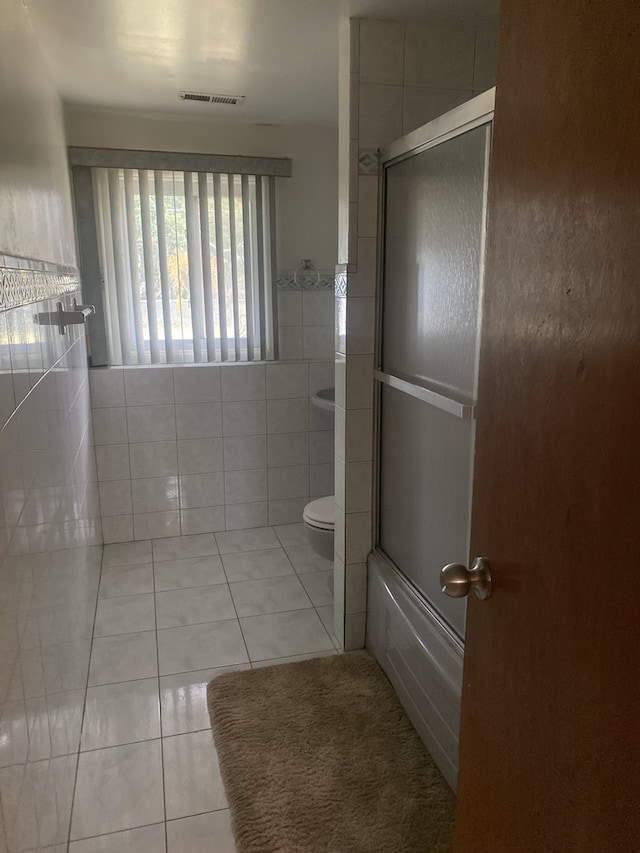 bathroom featuring toilet, tile patterned floors, tile walls, and enclosed tub / shower combo