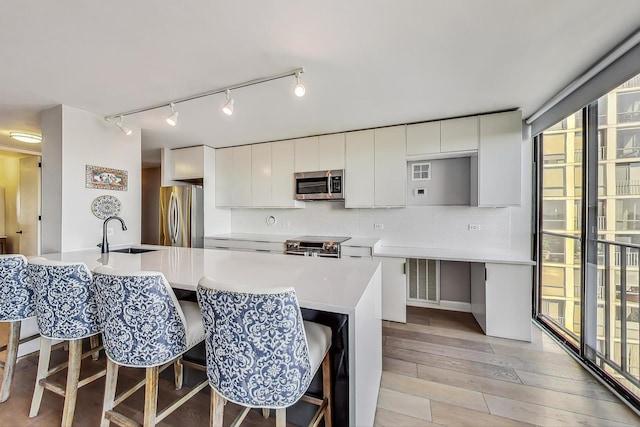 kitchen featuring a kitchen bar, light wood-style flooring, a sink, appliances with stainless steel finishes, and light countertops