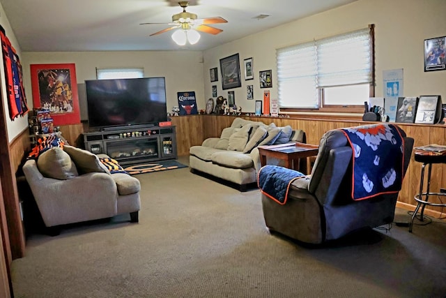 carpeted living room featuring ceiling fan and wood walls