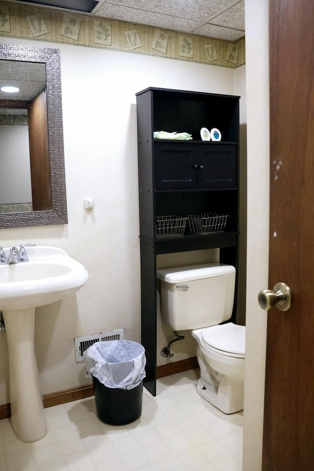 bathroom featuring a drop ceiling, toilet, and sink