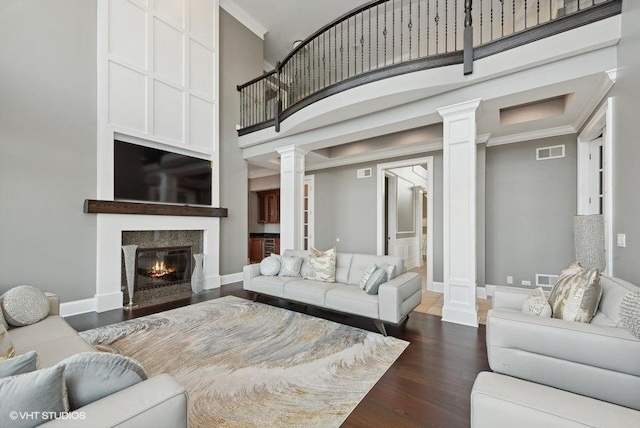 living room featuring decorative columns, a towering ceiling, dark wood-type flooring, and ornamental molding