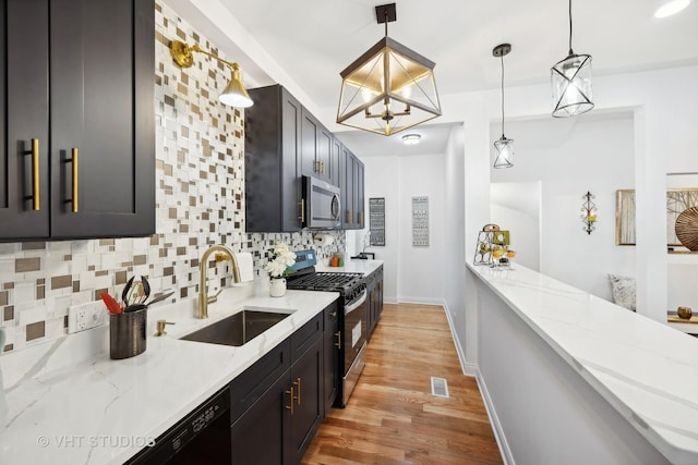 kitchen featuring light stone countertops, sink, hanging light fixtures, stainless steel appliances, and light wood-type flooring