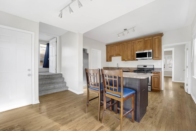 kitchen featuring light stone countertops, rail lighting, a breakfast bar area, appliances with stainless steel finishes, and hardwood / wood-style flooring