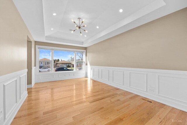 spare room with light hardwood / wood-style floors, a tray ceiling, and a notable chandelier