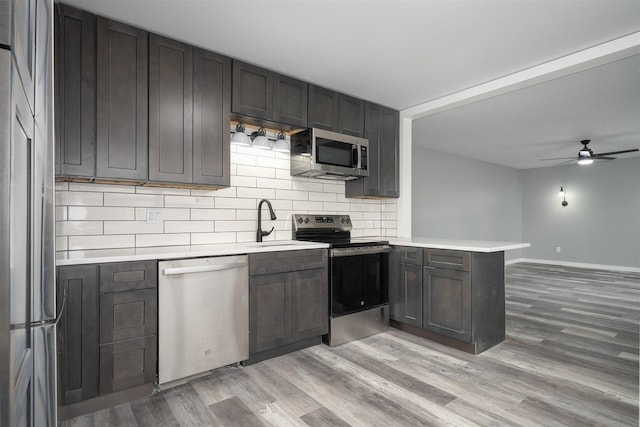 kitchen with decorative backsplash, light wood-type flooring, kitchen peninsula, and appliances with stainless steel finishes