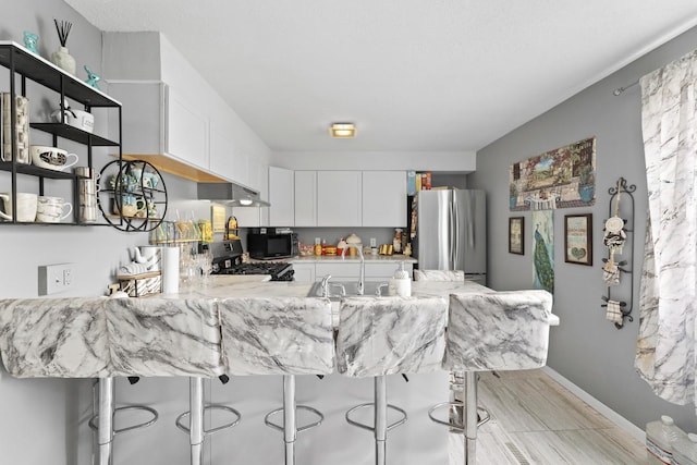 kitchen with white cabinetry, sink, black range oven, kitchen peninsula, and stainless steel fridge