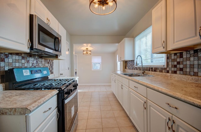 kitchen with backsplash, gas stove, sink, light tile patterned floors, and white cabinetry