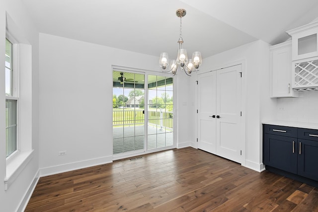 unfurnished dining area featuring dark wood-type flooring, lofted ceiling, and an inviting chandelier