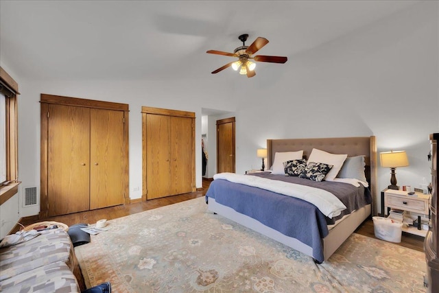 bedroom featuring ceiling fan, vaulted ceiling, light hardwood / wood-style flooring, and two closets