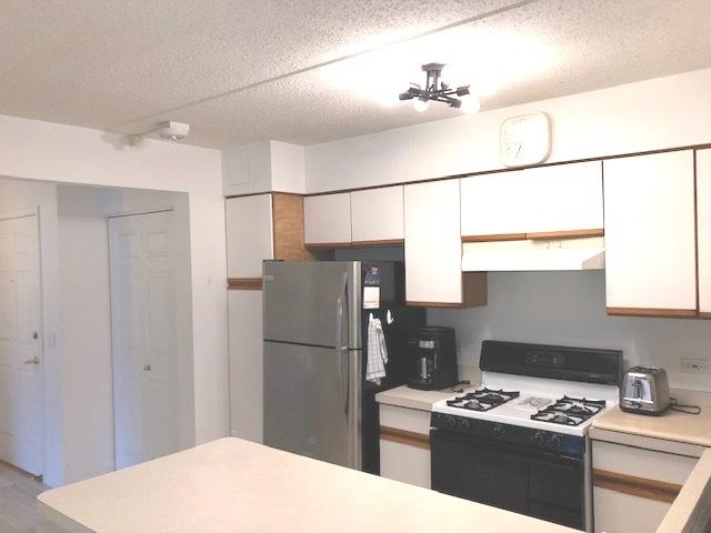 kitchen with stainless steel fridge, a textured ceiling, light hardwood / wood-style flooring, white range with gas stovetop, and white cabinetry