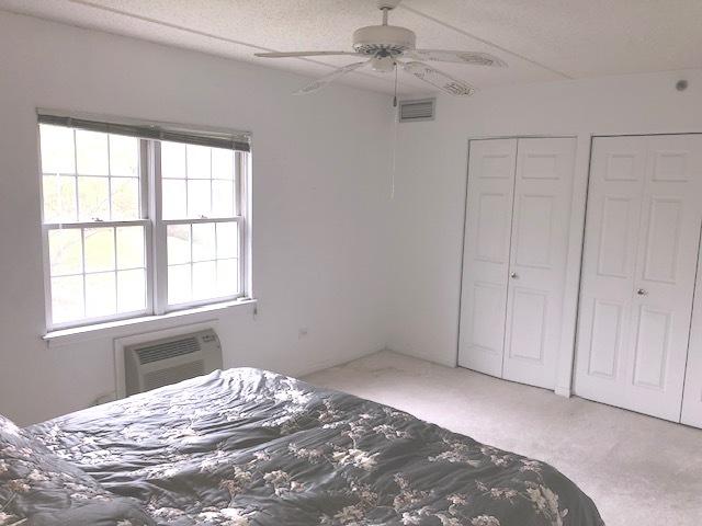 unfurnished bedroom with two closets, ceiling fan, a textured ceiling, carpet floors, and a wall unit AC