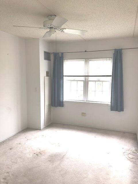 spare room with a textured ceiling, light colored carpet, and ceiling fan