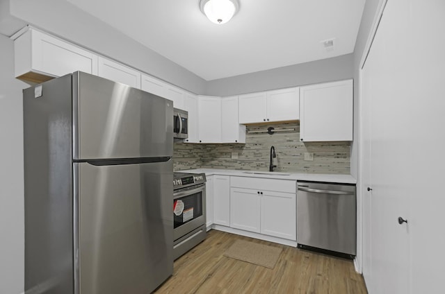 kitchen featuring appliances with stainless steel finishes, backsplash, sink, light hardwood / wood-style flooring, and white cabinets