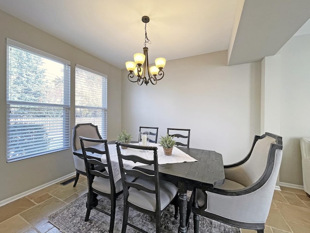 dining area featuring stone tile floors, visible vents, baseboards, and a chandelier