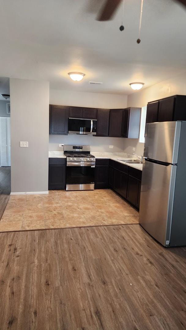 kitchen featuring dark brown cabinetry, sink, light hardwood / wood-style floors, and appliances with stainless steel finishes