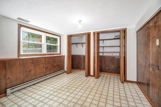 interior space featuring wooden walls, a baseboard radiator, and a textured ceiling