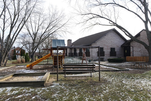 snow covered back of property featuring a playground