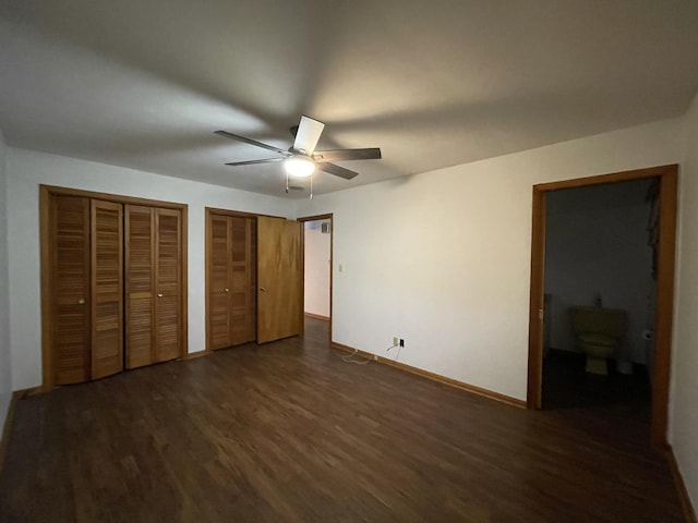 unfurnished bedroom with ceiling fan, dark wood-type flooring, and two closets