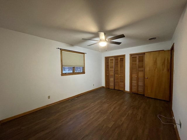 unfurnished bedroom with dark hardwood / wood-style flooring, ceiling fan, and multiple closets