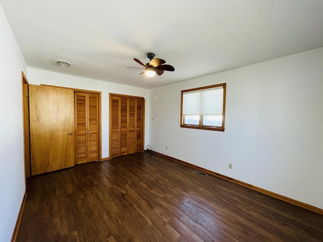 unfurnished bedroom with multiple closets, ceiling fan, and dark hardwood / wood-style floors