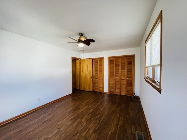 unfurnished bedroom with multiple closets, ceiling fan, and dark hardwood / wood-style floors