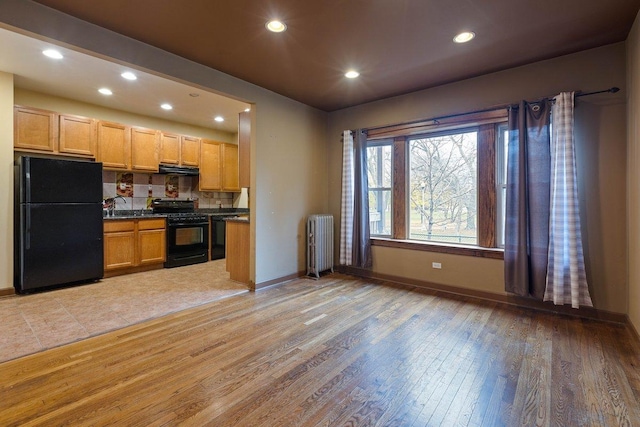 kitchen with sink, radiator heating unit, light brown cabinets, black appliances, and light wood-type flooring