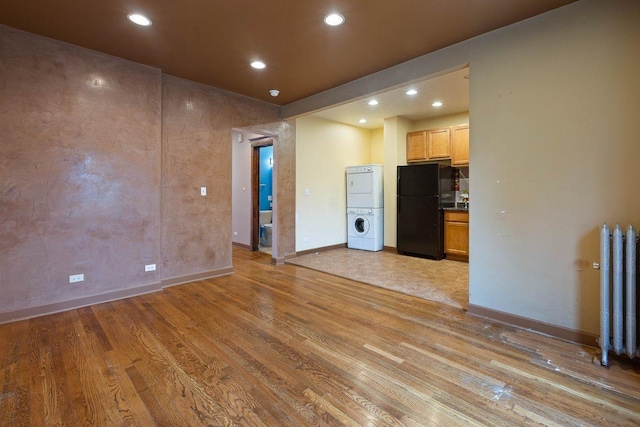 unfurnished living room with stacked washer / drying machine and light wood-type flooring