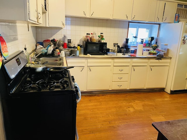 kitchen featuring sink, light wood-type flooring, white cabinetry, and black appliances