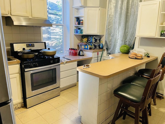 kitchen with a kitchen breakfast bar, decorative backsplash, white cabinetry, and appliances with stainless steel finishes