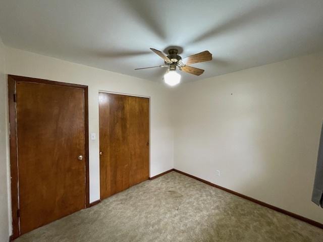 unfurnished bedroom with light colored carpet, ceiling fan, and multiple closets