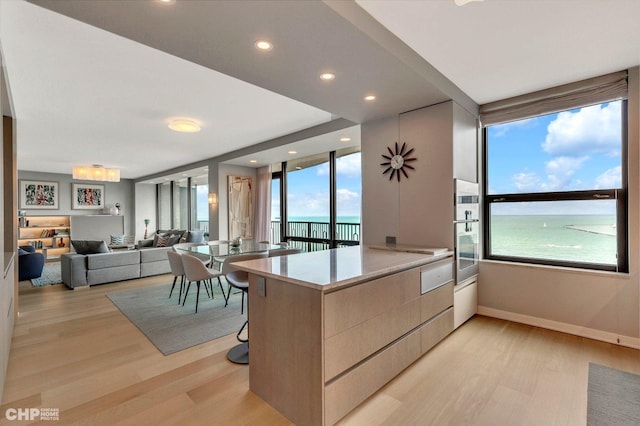 kitchen featuring light hardwood / wood-style floors, a water view, kitchen peninsula, and a breakfast bar area