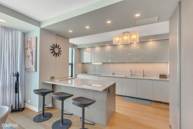 kitchen featuring black electric stovetop, a kitchen breakfast bar, sink, decorative backsplash, and light hardwood / wood-style floors