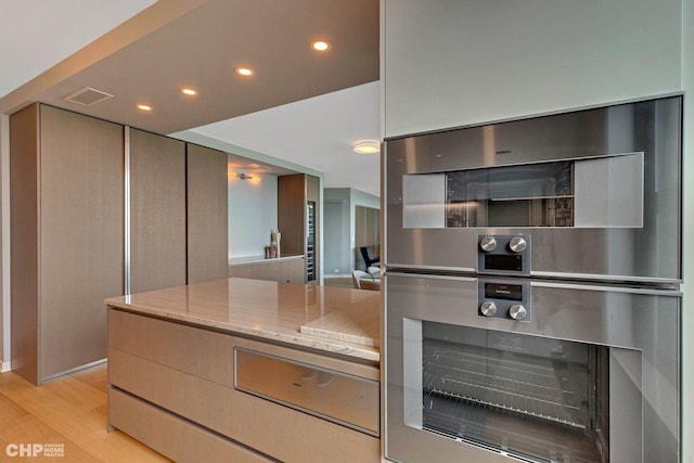 kitchen with light stone counters, double oven, and light hardwood / wood-style flooring