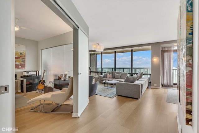 living room with a wall of windows, light hardwood / wood-style floors, and ceiling fan