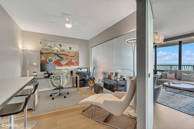 office area featuring ceiling fan, expansive windows, and light wood-type flooring