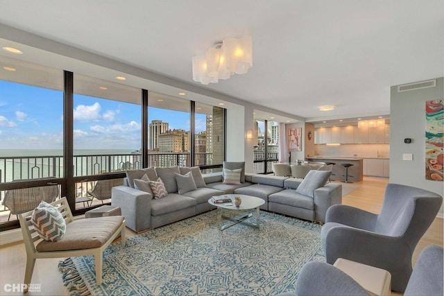 living room with a chandelier, light wood-type flooring, a water view, and a wall of windows