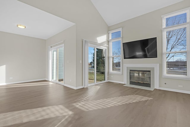 unfurnished living room with a tiled fireplace, wood-type flooring, plenty of natural light, and high vaulted ceiling