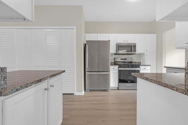 kitchen with light wood-type flooring, appliances with stainless steel finishes, dark stone counters, and white cabinets