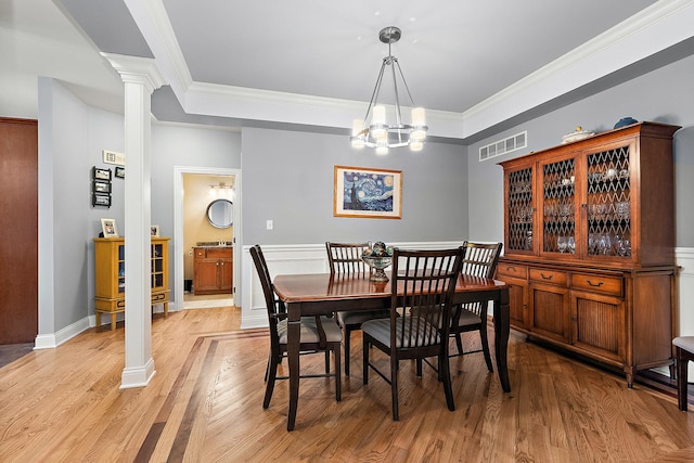 dining area with a chandelier, light wood-type flooring, decorative columns, and crown molding